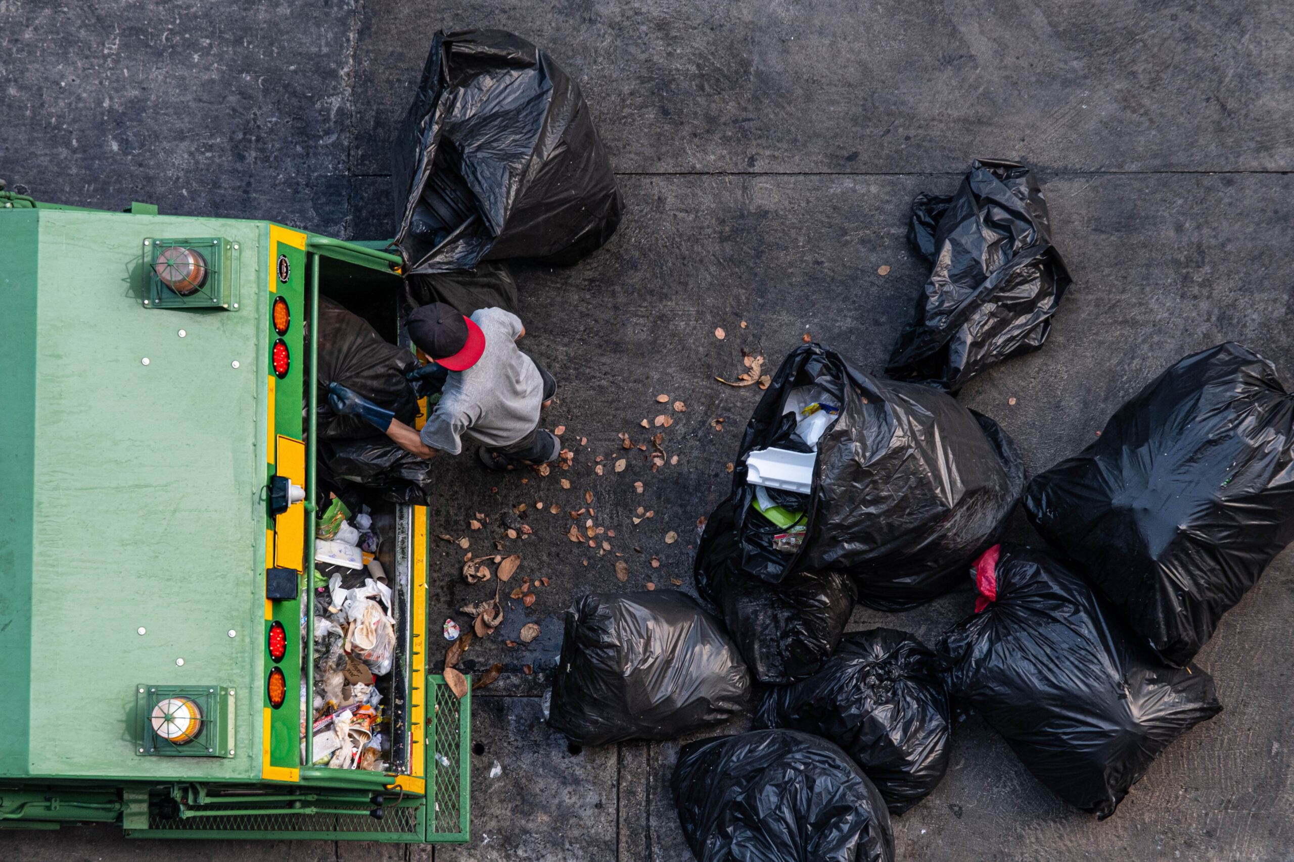Green garbage truck And the employees are collecting a lot of black garbage bags that are tied up On the sidewalk To discard Viewed from the top view on 06/02/2020 Bangkok Noi, Bangkok. Thailand